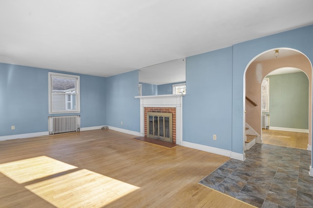 unfurnished living room with wood-type flooring, radiator heating unit, and a brick fireplace