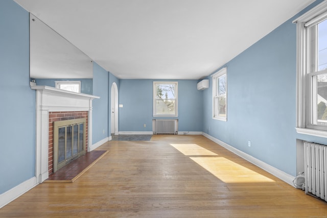 unfurnished living room with vaulted ceiling, radiator heating unit, a fireplace, and an AC wall unit