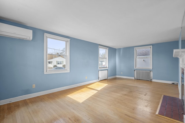 unfurnished living room with a wall unit AC, radiator heating unit, light wood-type flooring, and a brick fireplace