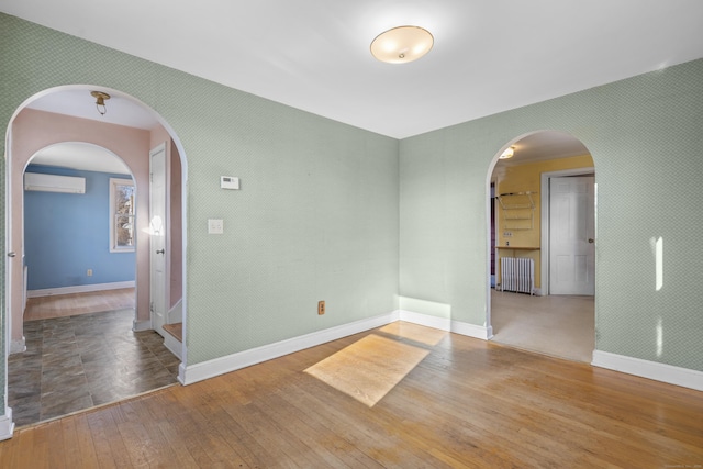 empty room with a wall mounted air conditioner, wood-type flooring, and radiator