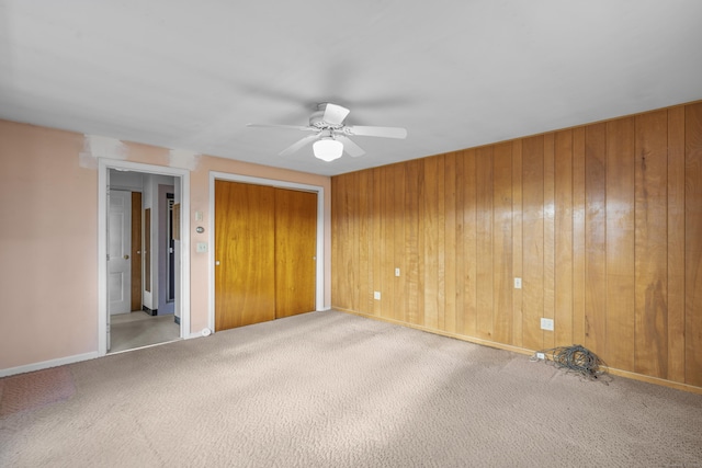 unfurnished bedroom featuring carpet, wood walls, a closet, and ceiling fan