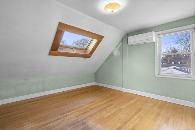 additional living space with vaulted ceiling with skylight, a wall unit AC, and light hardwood / wood-style flooring