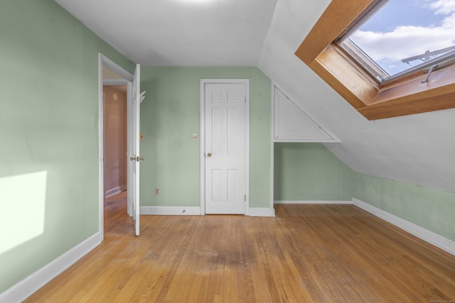 additional living space with light wood-type flooring and vaulted ceiling with skylight