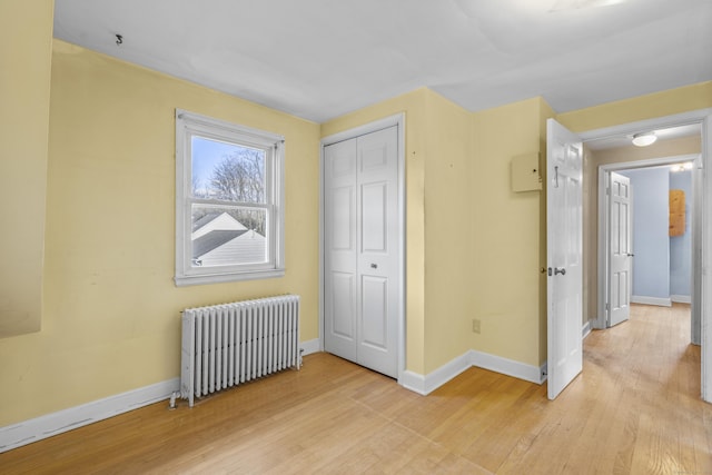 unfurnished bedroom with radiator, a closet, and light wood-type flooring