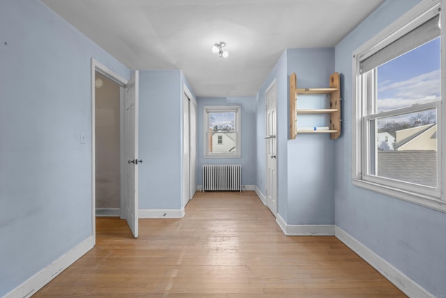 hallway with radiator, light hardwood / wood-style flooring, and a healthy amount of sunlight