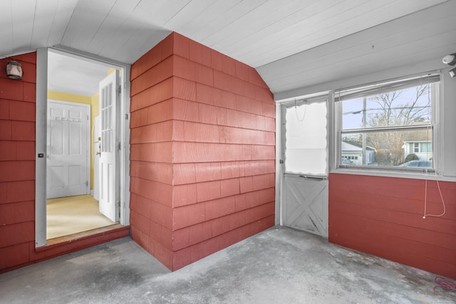 interior space featuring lofted ceiling, wooden walls, and concrete flooring