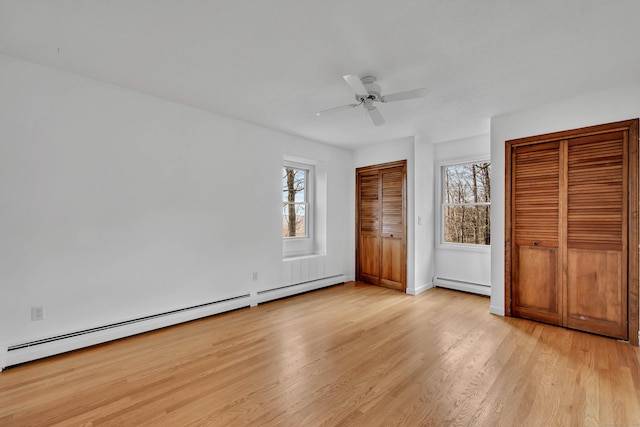 unfurnished bedroom featuring two closets, ceiling fan, a baseboard heating unit, and light hardwood / wood-style floors