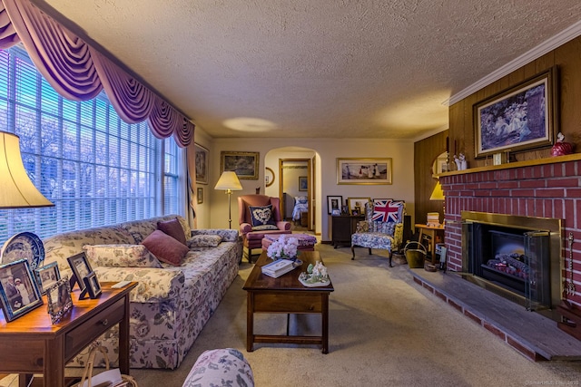 living room with crown molding, wooden walls, a brick fireplace, a textured ceiling, and carpet floors