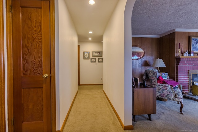 hallway with wood walls, crown molding, light colored carpet, and a textured ceiling