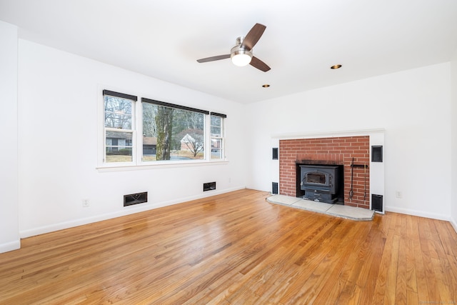 unfurnished living room featuring a wood stove, ceiling fan, and light hardwood / wood-style flooring