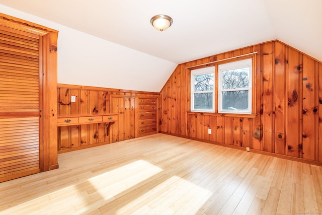 additional living space featuring light hardwood / wood-style floors, wooden walls, and vaulted ceiling