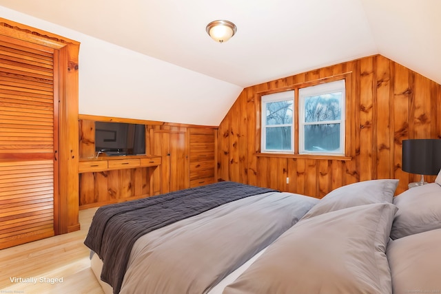 bedroom featuring light hardwood / wood-style floors, vaulted ceiling, and wood walls