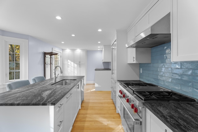 kitchen featuring white cabinetry, sink, wall chimney range hood, dark stone counters, and high end stainless steel range