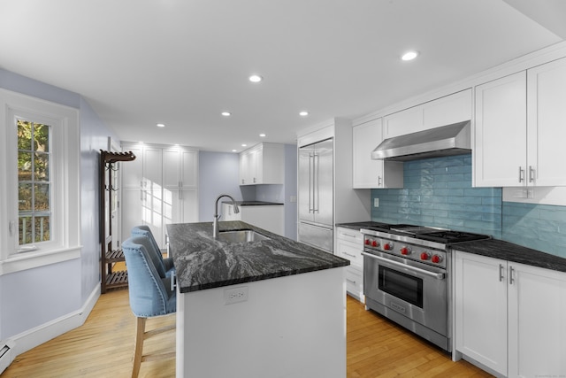 kitchen with a kitchen island with sink, white cabinets, luxury range, and extractor fan