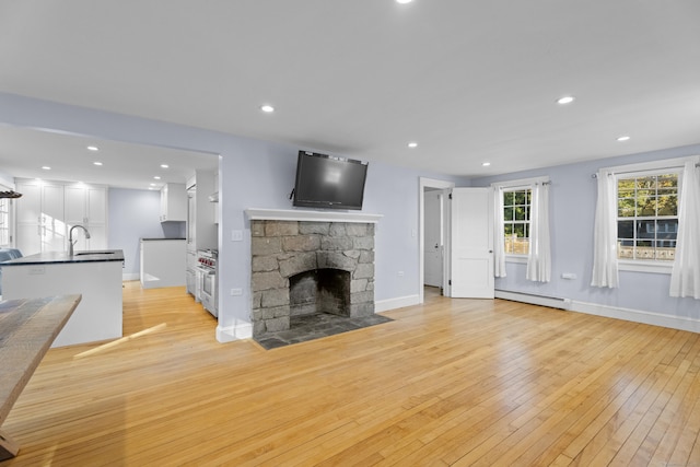 unfurnished living room with a fireplace, light hardwood / wood-style floors, a baseboard heating unit, and sink