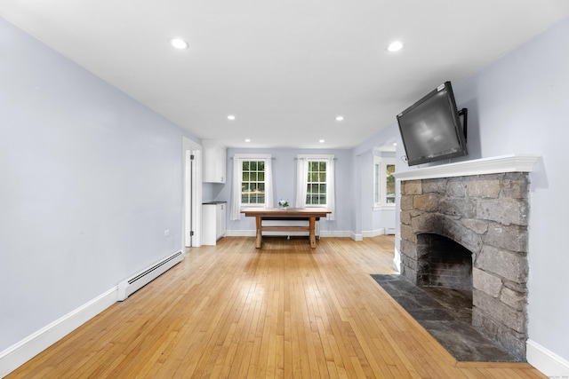 unfurnished living room featuring a fireplace, light wood-type flooring, and a baseboard heating unit