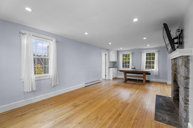 unfurnished living room featuring a healthy amount of sunlight, a fireplace, a baseboard radiator, and light wood-type flooring