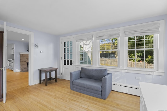 living area featuring a fireplace, light hardwood / wood-style flooring, and a baseboard heating unit