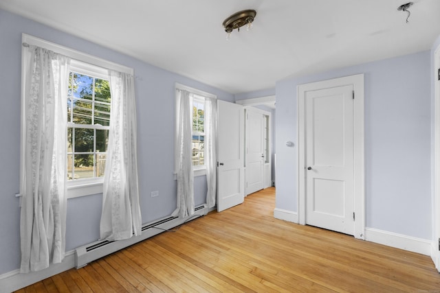 empty room featuring a wealth of natural light, light hardwood / wood-style flooring, and a baseboard heating unit