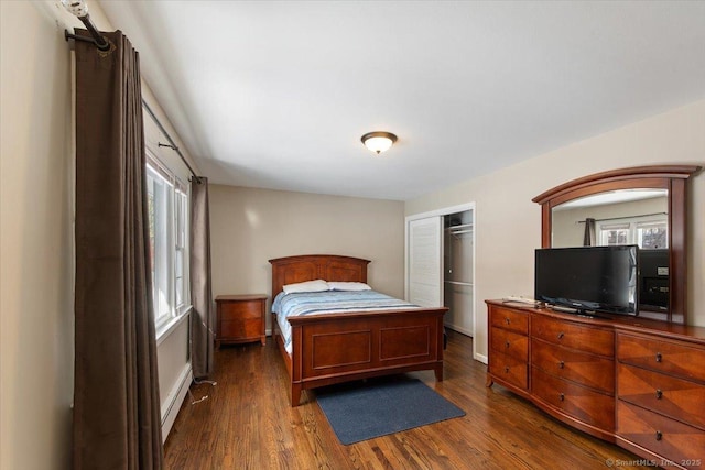 bedroom with dark hardwood / wood-style floors, a baseboard heating unit, and a closet