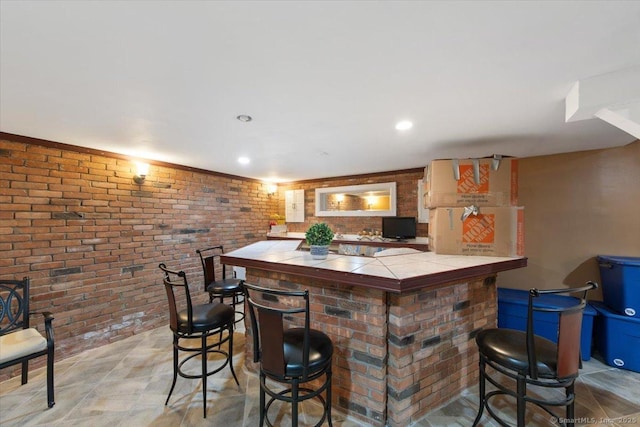 bar with tile countertops and brick wall