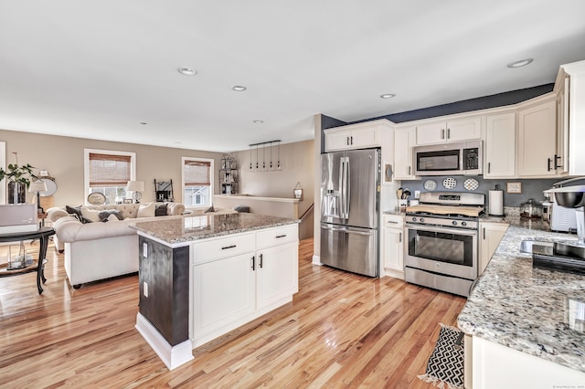 kitchen featuring light stone countertops, white cabinetry, stainless steel appliances, and light wood-type flooring