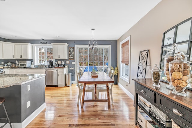 kitchen with white cabinetry, hanging light fixtures, an inviting chandelier, light stone counters, and stainless steel dishwasher