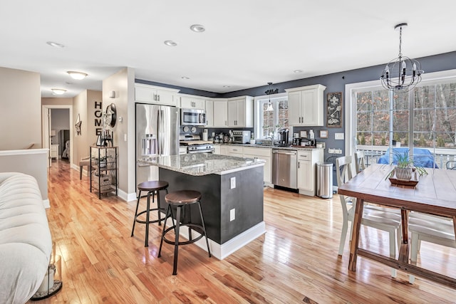 kitchen featuring stainless steel appliances, decorative light fixtures, white cabinets, light hardwood / wood-style floors, and a kitchen island