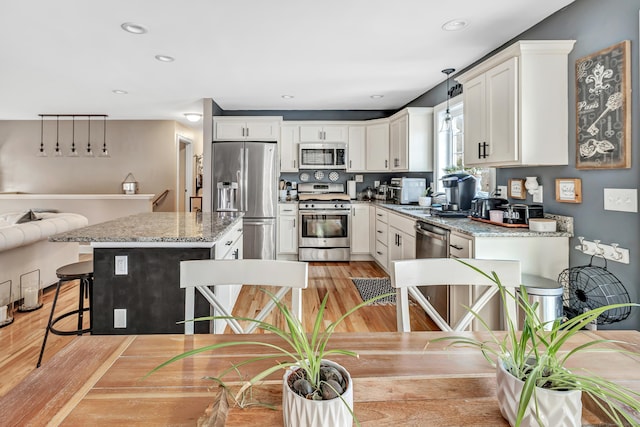 kitchen featuring light stone countertops, pendant lighting, a breakfast bar, a kitchen island, and appliances with stainless steel finishes