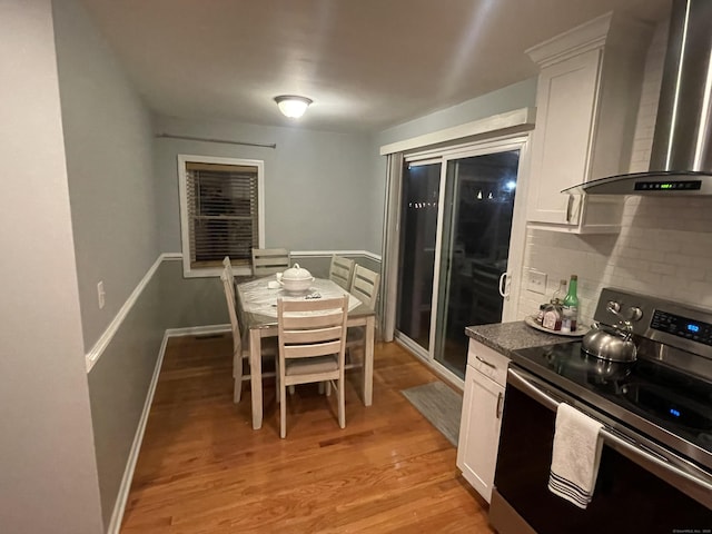 kitchen with stainless steel electric range, white cabinetry, wall chimney range hood, and light hardwood / wood-style flooring