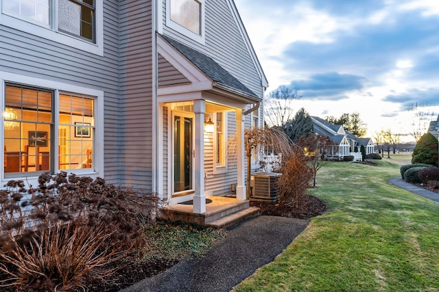 exterior entry at dusk with central AC unit and a lawn