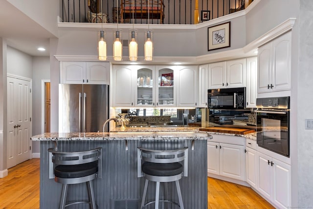 kitchen with black appliances, a kitchen breakfast bar, white cabinetry, and a kitchen island with sink