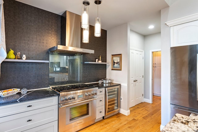 kitchen featuring appliances with stainless steel finishes, wall chimney range hood, decorative light fixtures, white cabinetry, and wine cooler