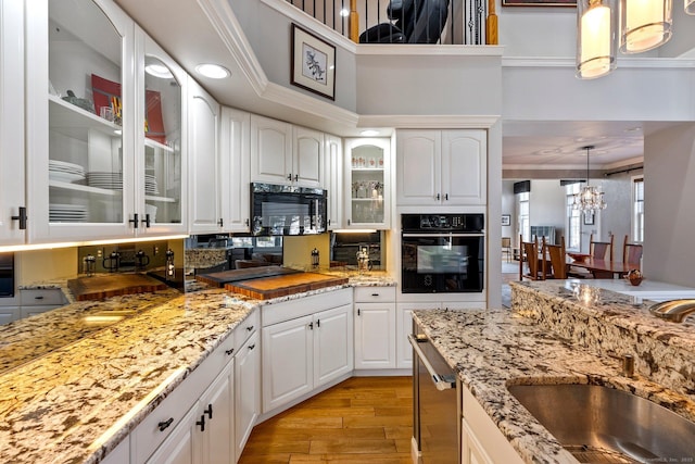 kitchen with sink, black appliances, light hardwood / wood-style flooring, white cabinets, and hanging light fixtures