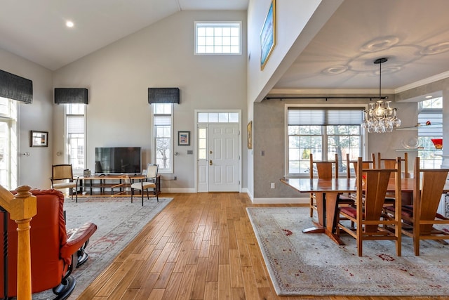 foyer entrance with ornamental molding, a towering ceiling, light hardwood / wood-style floors, and a notable chandelier