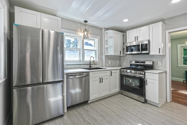 kitchen featuring white cabinets, stainless steel appliances, light hardwood / wood-style floors, sink, and hanging light fixtures