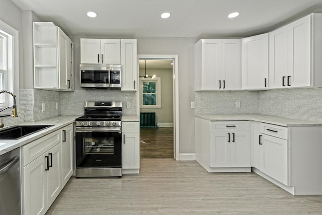 kitchen with white cabinets, radiator heating unit, stainless steel appliances, sink, and light wood-type flooring