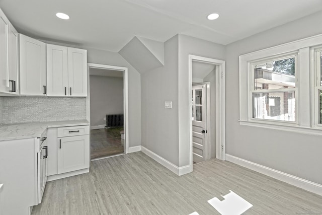 kitchen featuring decorative backsplash, white cabinetry, radiator heating unit, and light hardwood / wood-style flooring