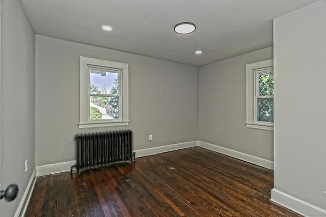 unfurnished room with dark wood-type flooring, plenty of natural light, and radiator heating unit