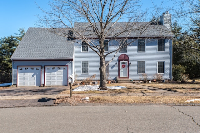 colonial home with a garage, driveway, a chimney, and roof with shingles