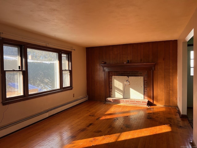 unfurnished living room featuring hardwood / wood-style flooring, a baseboard heating unit, a fireplace, and wood walls