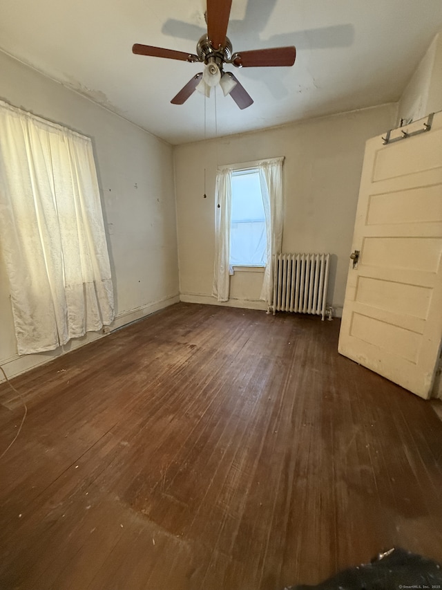 empty room featuring dark hardwood / wood-style flooring, ceiling fan, and radiator heating unit