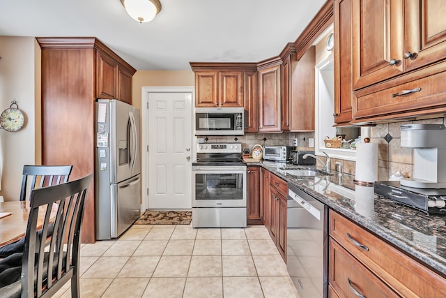 kitchen with appliances with stainless steel finishes, backsplash, sink, light tile patterned floors, and dark stone countertops