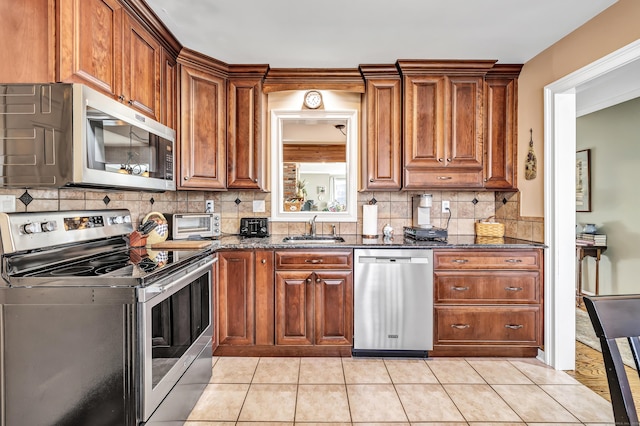 kitchen featuring sink, decorative backsplash, dark stone countertops, light tile patterned floors, and appliances with stainless steel finishes