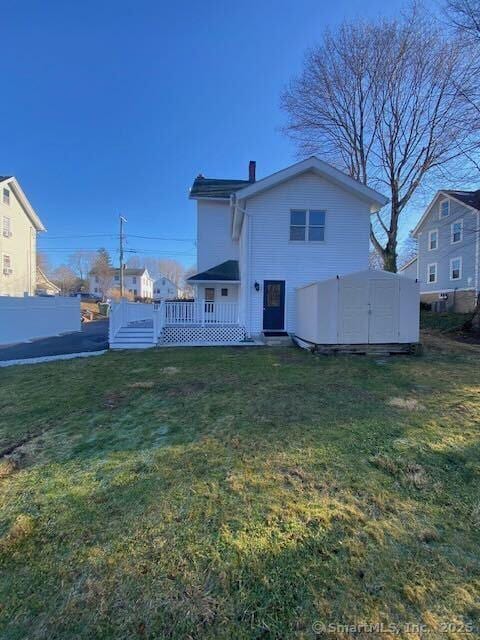 back of house with a lawn, a storage shed, and a deck