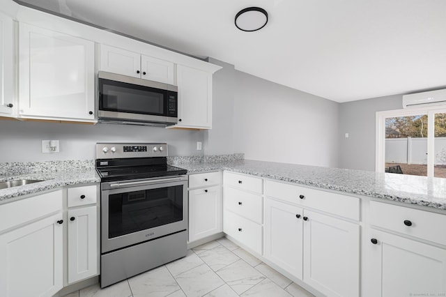 kitchen with stainless steel appliances, light stone counters, an AC wall unit, kitchen peninsula, and white cabinets