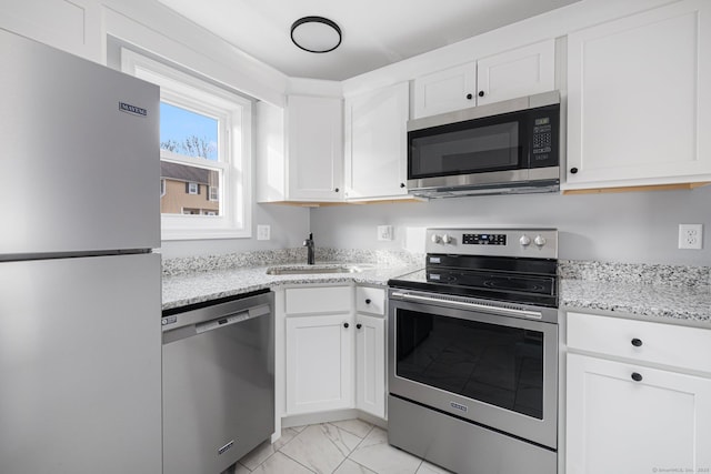 kitchen with white cabinets, appliances with stainless steel finishes, light stone countertops, and sink