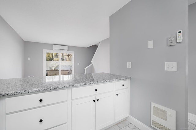 kitchen with white cabinets, heating unit, light stone counters, and a wall unit AC