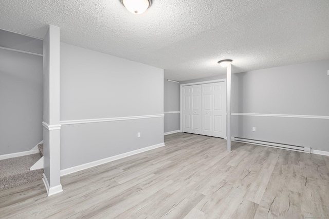 basement featuring a textured ceiling, a baseboard radiator, and light hardwood / wood-style flooring