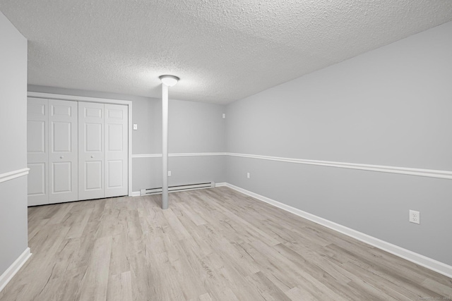 basement featuring a textured ceiling, light hardwood / wood-style flooring, and a baseboard heating unit